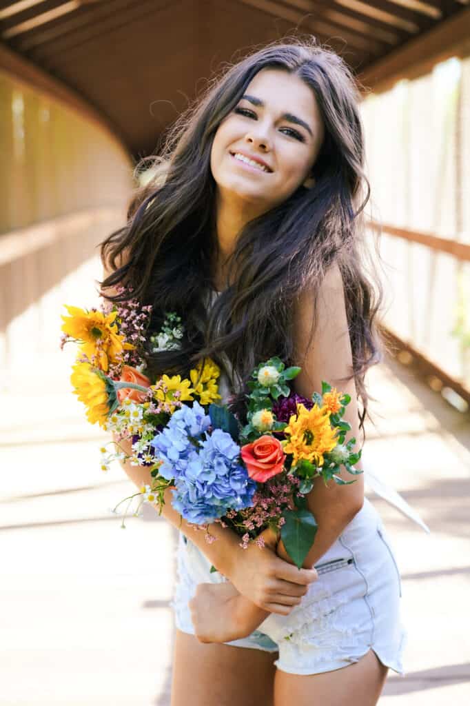 A young woman holding a bouquet of flowers on a bridge.