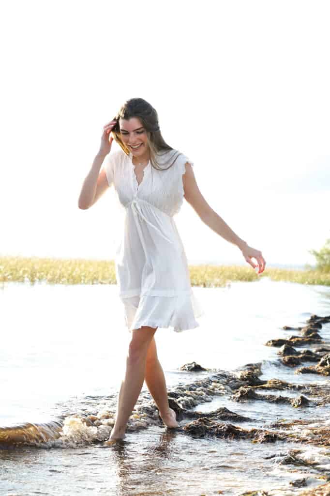 A woman in a white dress walking in shallow water.