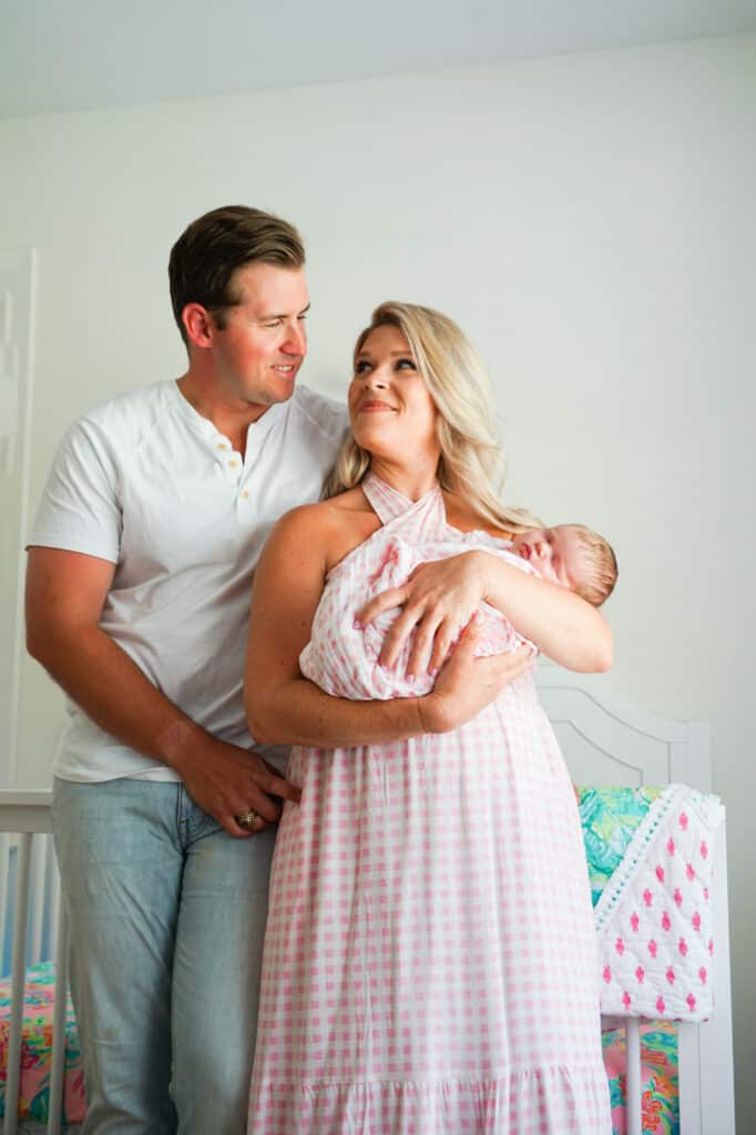 A man and woman holding a baby in a pink dress.