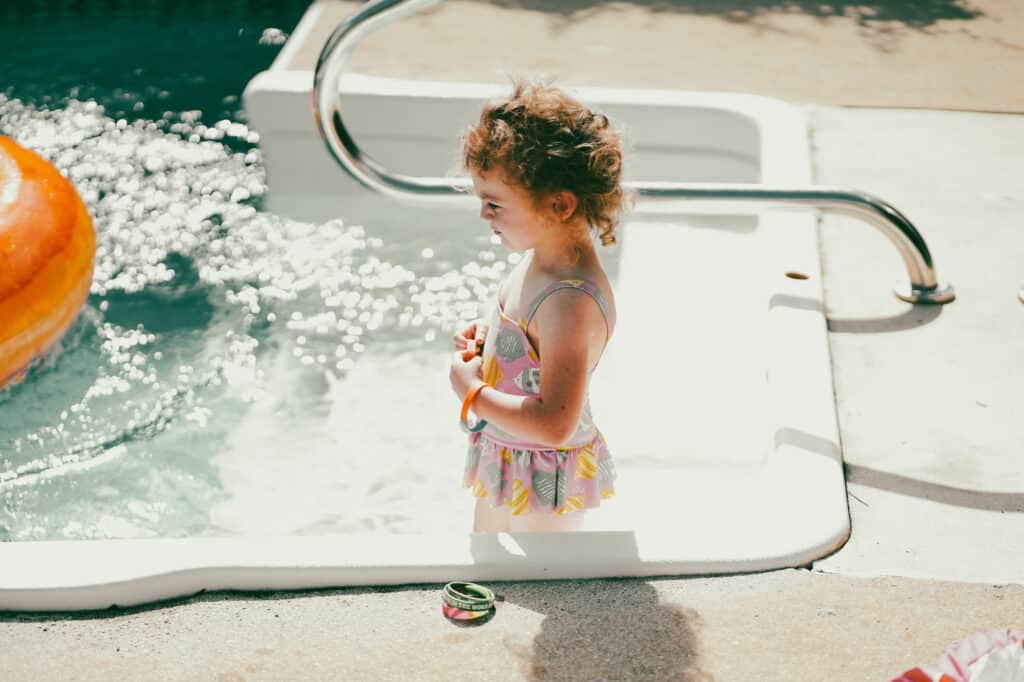 A little girl in a swimsuit standing next to a pool.