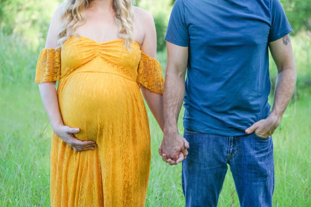 A pregnant couple holding hands in a field.