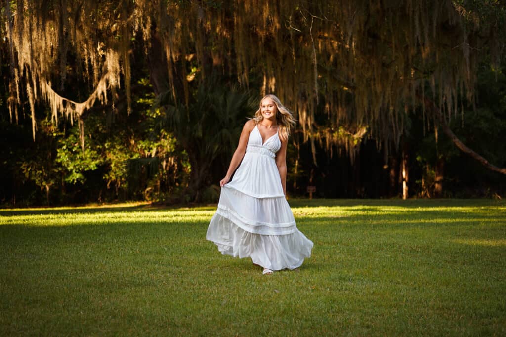 A woman in a white dress standing in a field with spanish moss.