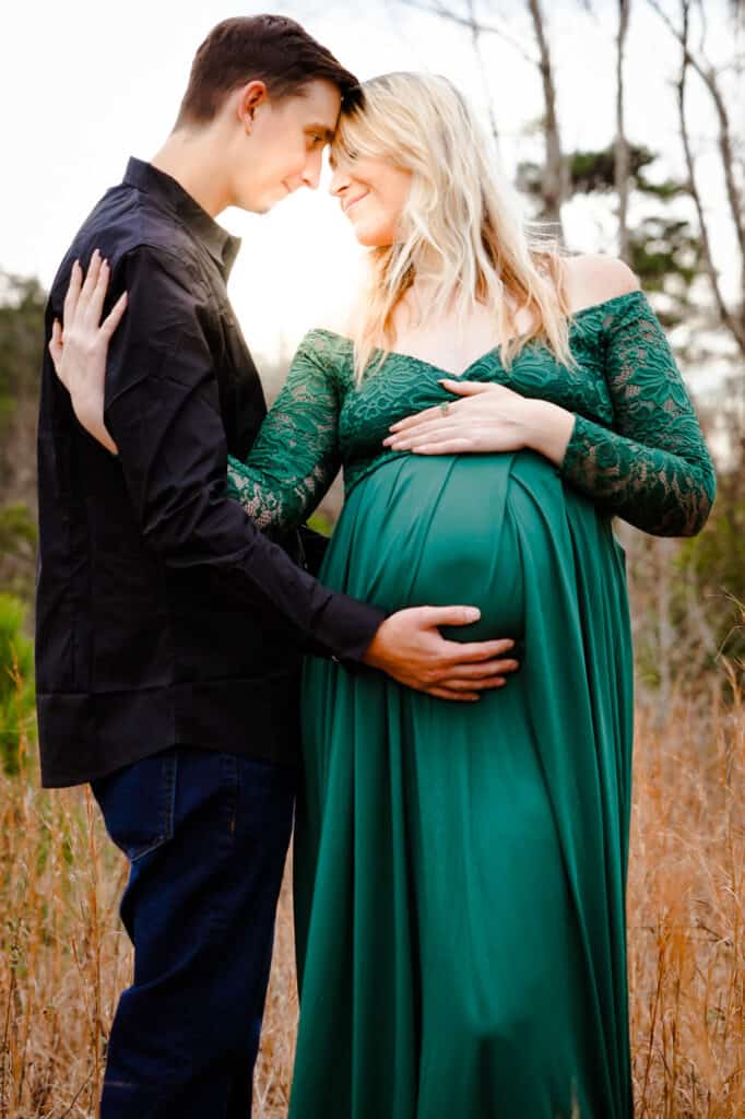 A pregnant couple in a green dress embracing in a field.