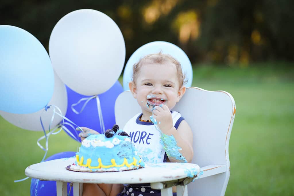 A baby sitting in a high chair eating a birthday cake.