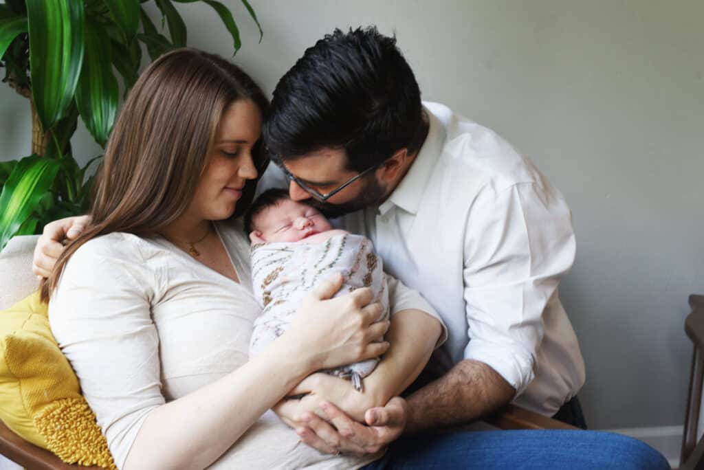 A man and woman kissing their newborn baby in a living room.