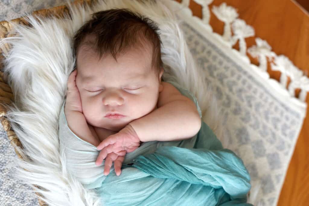 A baby sleeping in a blue blanket on a white rug.