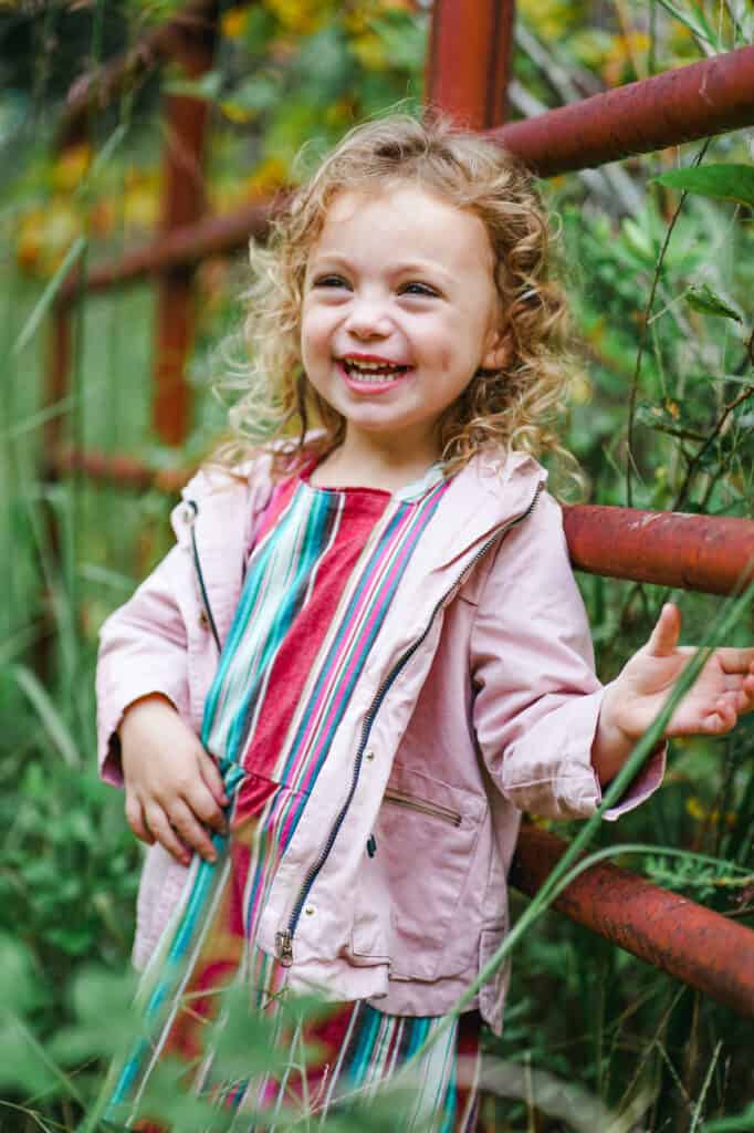 A little girl in a pink dress standing next to a fence.
