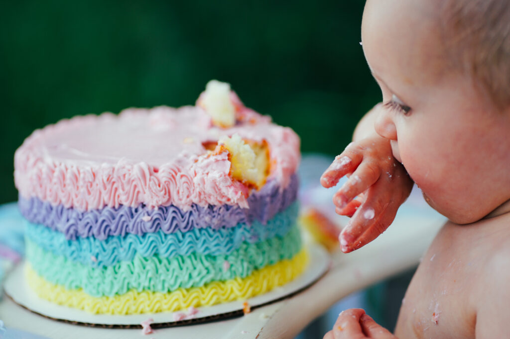 A baby is eating a rainbow cake.