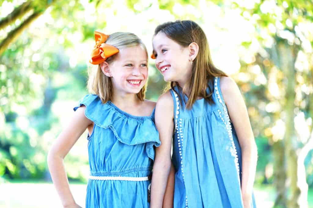 Two little girls wearing blue dresses and orange bows.