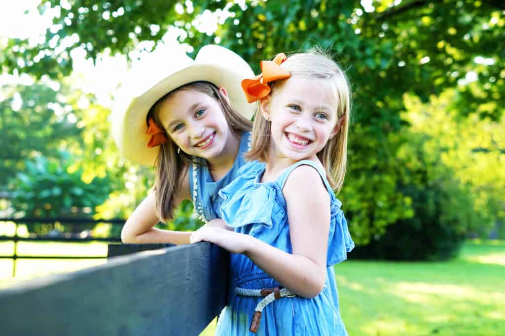 Two girls in cowboy hats leaning against a fence.