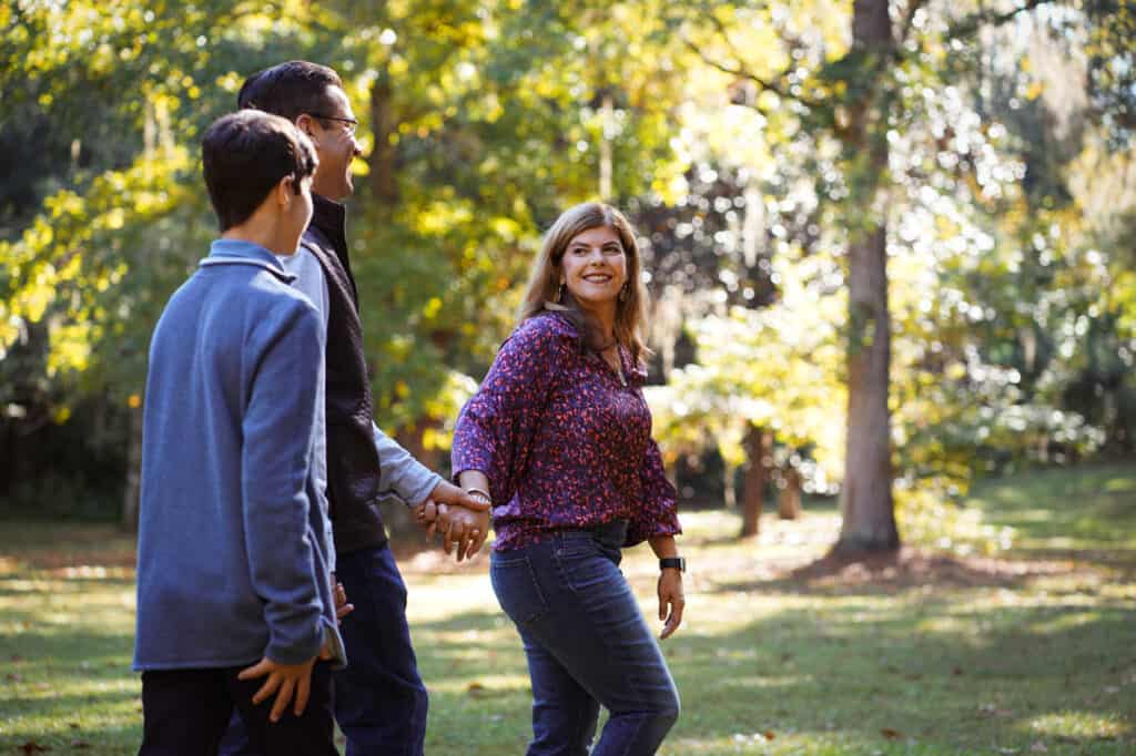 Three people walking in a park holding hands.