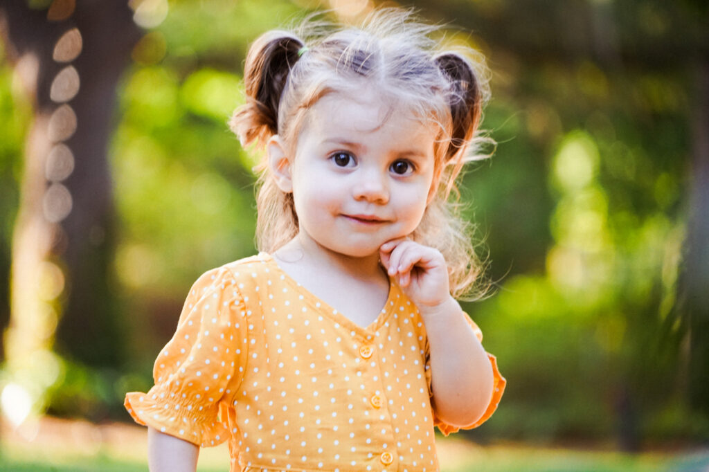 A little girl in an orange polka dot dress standing in a park.