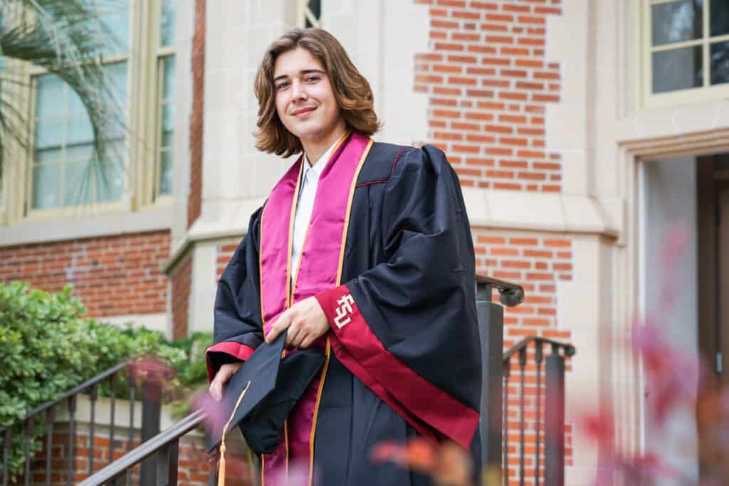 A young man in a graduation gown standing on steps.