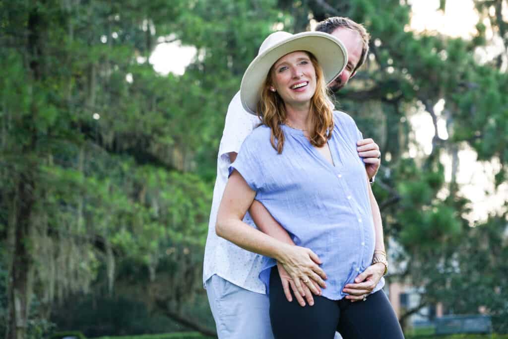 A pregnant woman is hugging a man in a park.