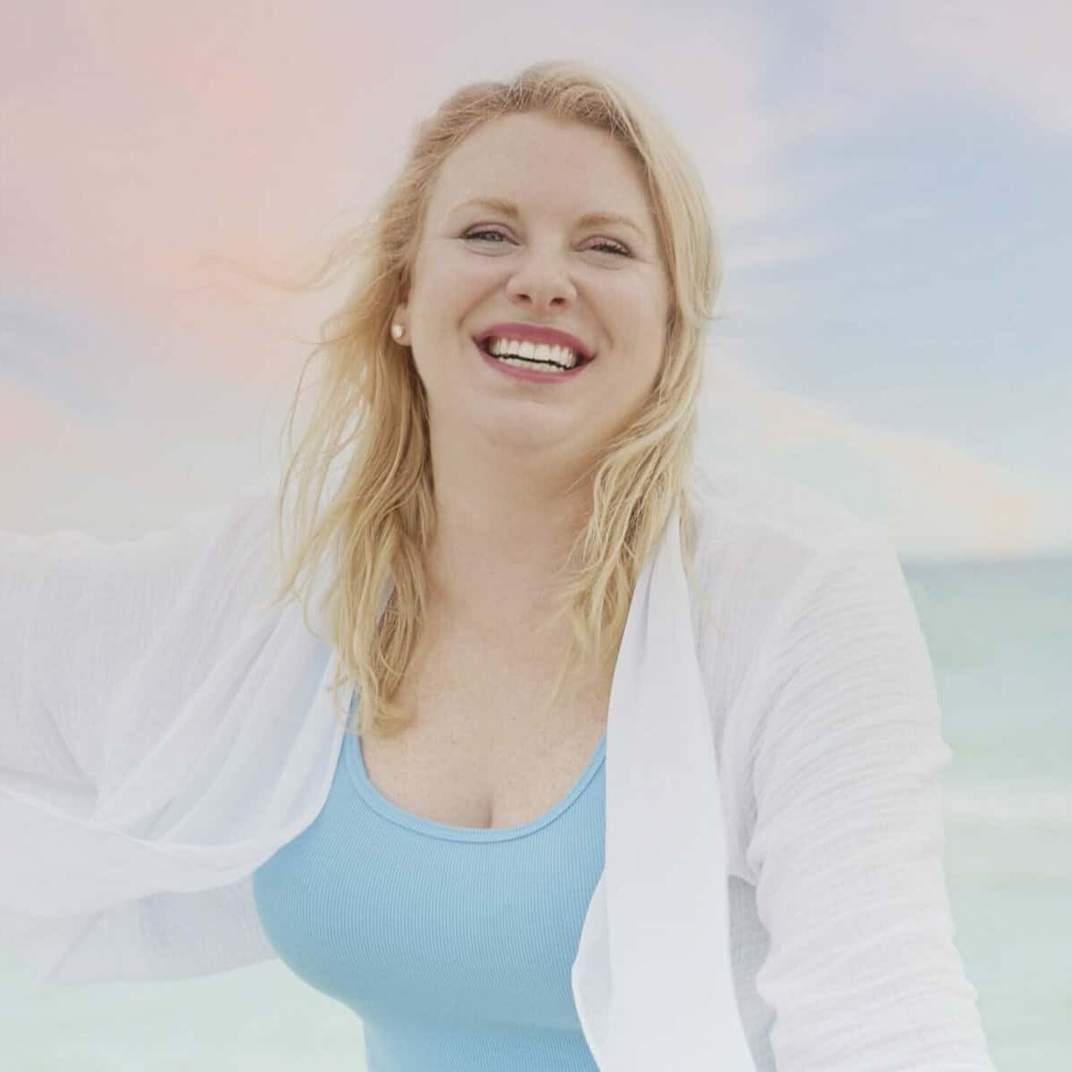 A smiling woman in a blue swimsuit on the beach.